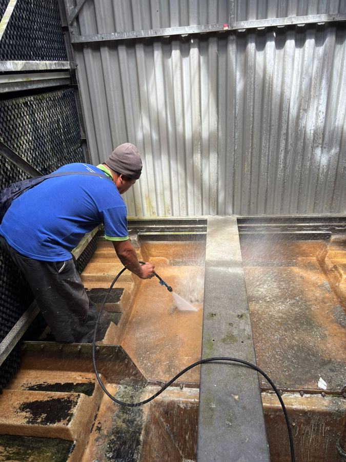 Technician pressure-washing a mall cooling tower